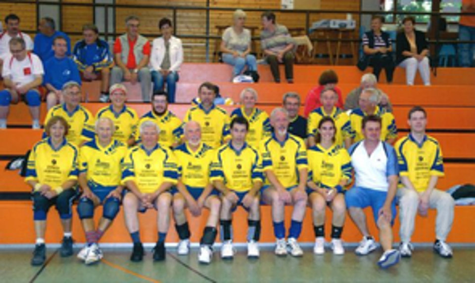 Gruppenfoto einer Volleyballmannschaft mit ca. 15 Personen in gelben Trikots, auf einer Tribüne sitzend
