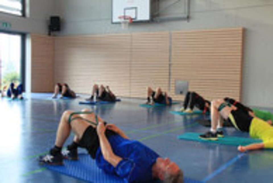10 Personen bei Bodengymnastik in Turnhalle